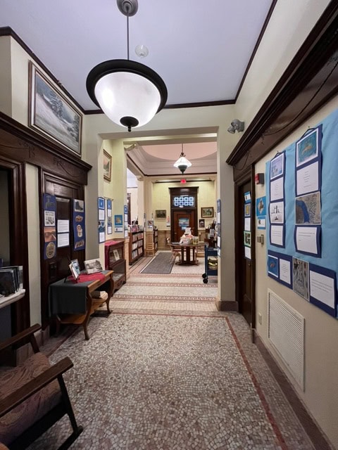 hallway of a library with displays on the walls, leading to a reading area with bookshelves, tables, and people seated in the background.