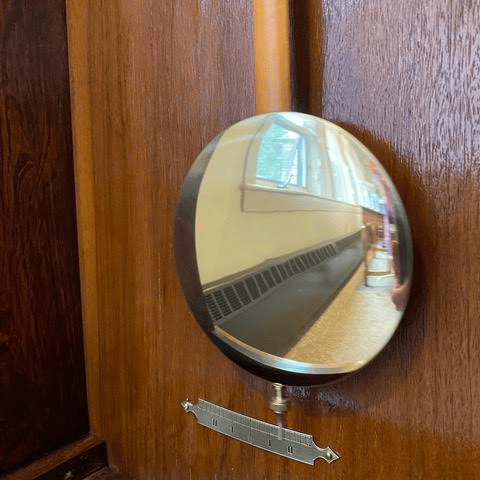 a round, reflective gauge is mounted on a wooden wall, showing a distorted reflection of a window and part of a hallway.