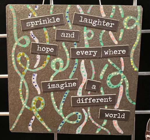 a decorative sign with the phrases "sprinkle laughter and hope everywhere, imagine a different world" over a background of colorful swirling lines.
