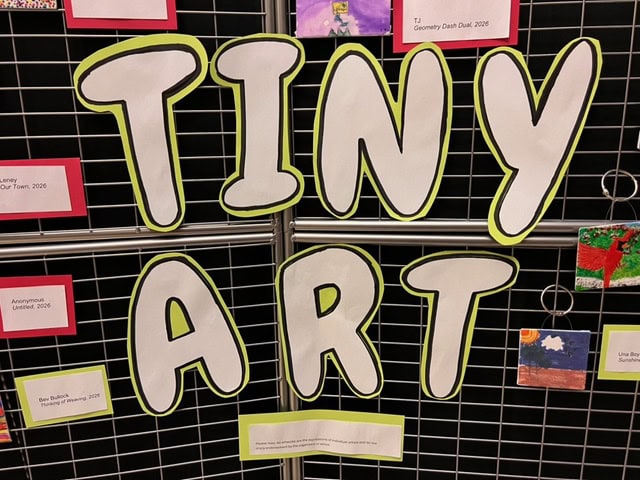 a display board with large letters spelling "tiny art," surrounded by small pieces of artwork and labels.