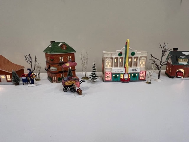 a miniature winter village display with small buildings, trees, a popcorn cart, and figurines arranged on a white surface.
