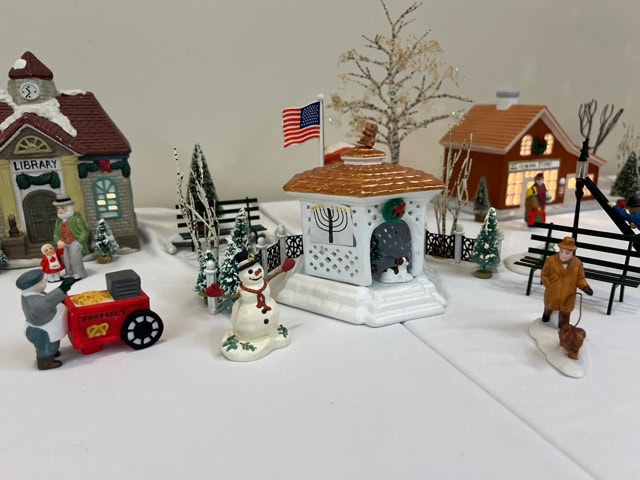 miniature winter village scene with small buildings, snowmen, trees, a gazebo with an american flag, and figurines including a man with a dog and a person with a cart.