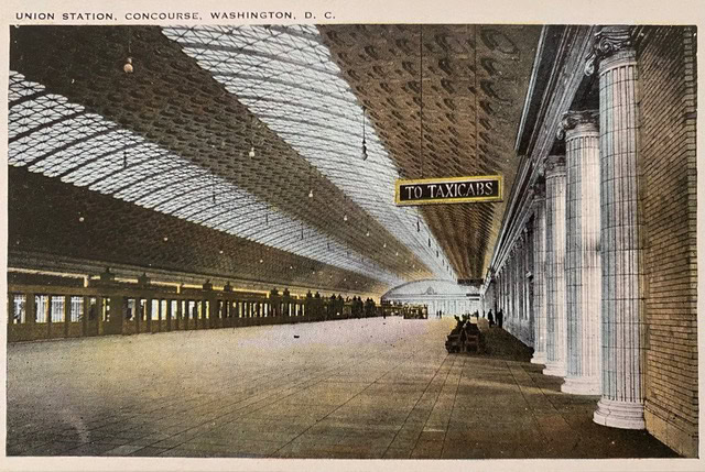 wide concourse at union station, washington, d.c., with a glass ceiling, large columns, and a hanging sign directing people "to taxicabs.