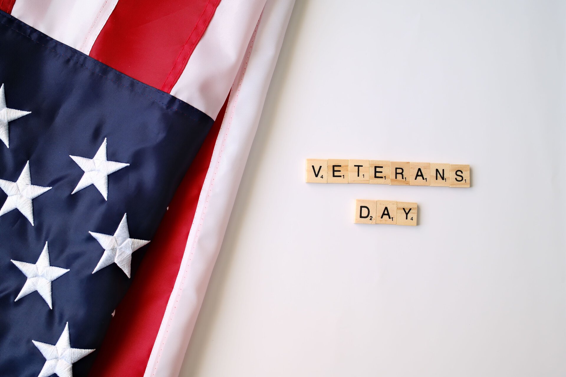 an american flag beside scrabble tiles that spell “veterans day.”