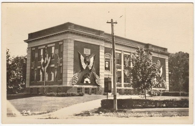 a large brick building decorated with patriotic banners and an eagle, labeled "high school williamsburg, mass." stands amid trees and a lawn.