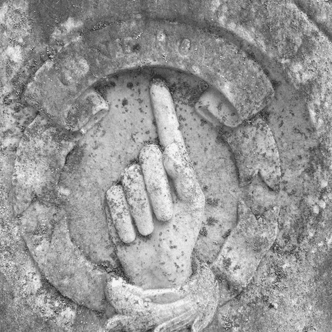 weathered stone carving of an upward pointing hand with a finger extended, set within a circular border on a textured surface.