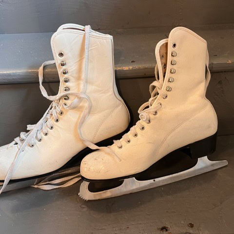 a pair of white figure skates with black soles and long laces placed on gray steps.