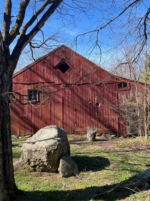 a weathered red barn stands behind rocks and leafless trees under a clear blue sky on a sunny day.