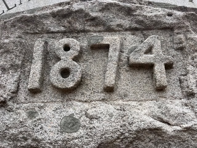close up of the number "1874" engraved in raised stone on a weathered rock surface.