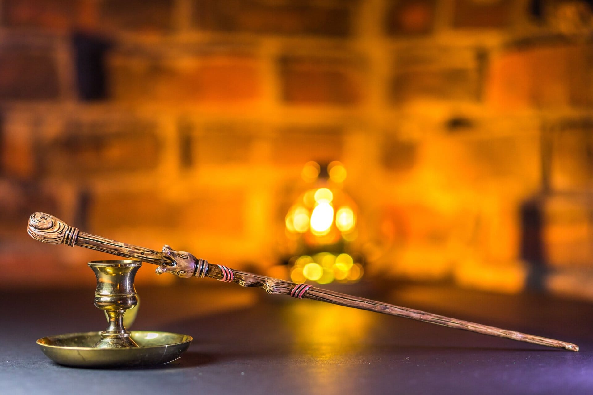 a brass candlestick holds a candle snuffer with a wooden handle, set on a dark surface against a blurred brick background.