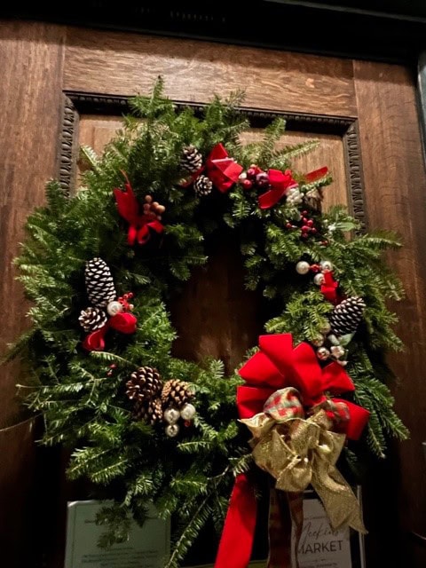 a green holiday wreath decorated with pinecones, red berries, and red bows hangs on a wooden door.