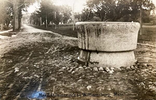 a stone water trough on a dirt road lined with trees in williamsburg, massachusetts, with engraving and a note of the donor at the base.