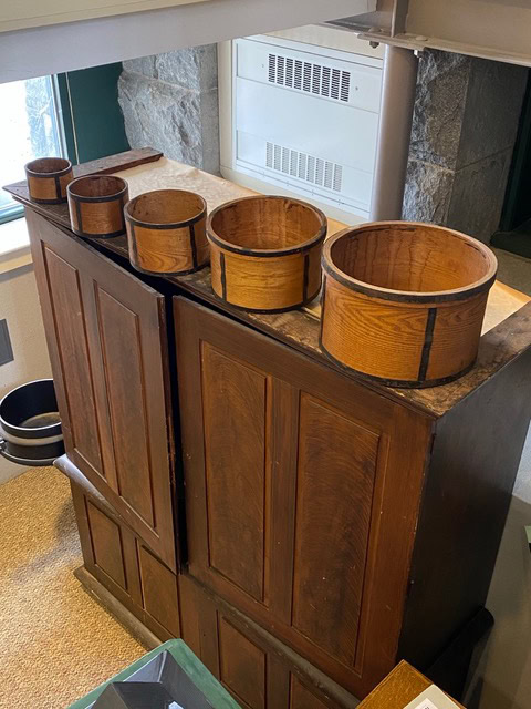 five wooden containers of varying sizes rest on top of a dark wooden cabinet in a well lit indoor setting.
