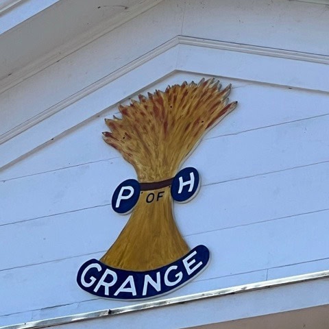 a sign with a bundle of wheat labeled "p of h grange" is mounted on the exterior of a white building.