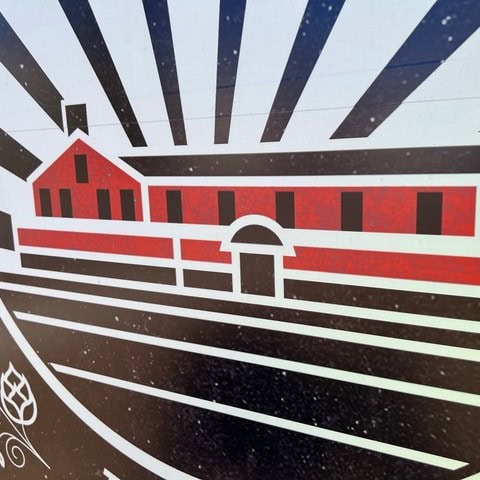 stylized illustration of a red building with black windows and lines radiating outward, resembling sun rays, over a black and white striped background.