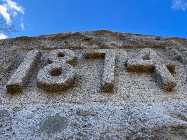 close up view of the year "1874" carved into a stone monument, with a blue sky in the background.
