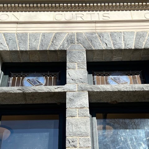 upper portion of a stone building facade showing two stained glass windows and engraved text reading "curtis.