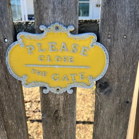 a yellow sign on a wooden gate reads "please close the gate" in capital letters.