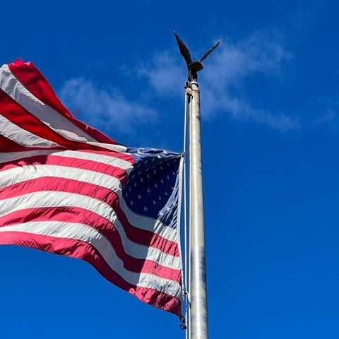 the american flag waves on a flagpole topped with an eagle ornament against a clear blue sky.