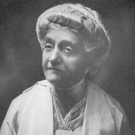 elderly woman with curly hair wears a hat and light colored clothing, looking slightly to the side in a black and white portrait.