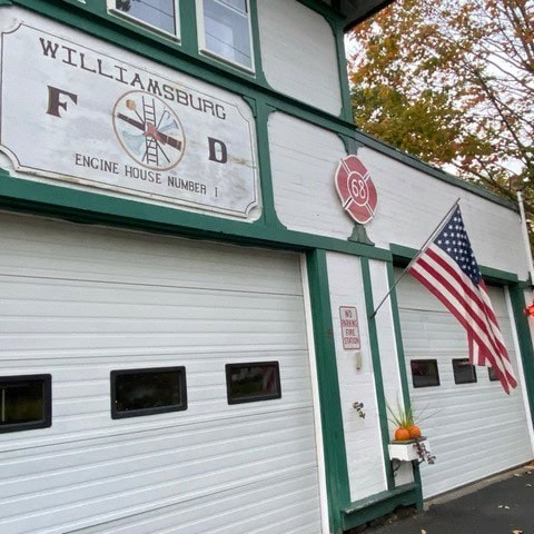 williamsburg fire department engine house number 1, white and green building with american flag and fire department insignia above garage doors.