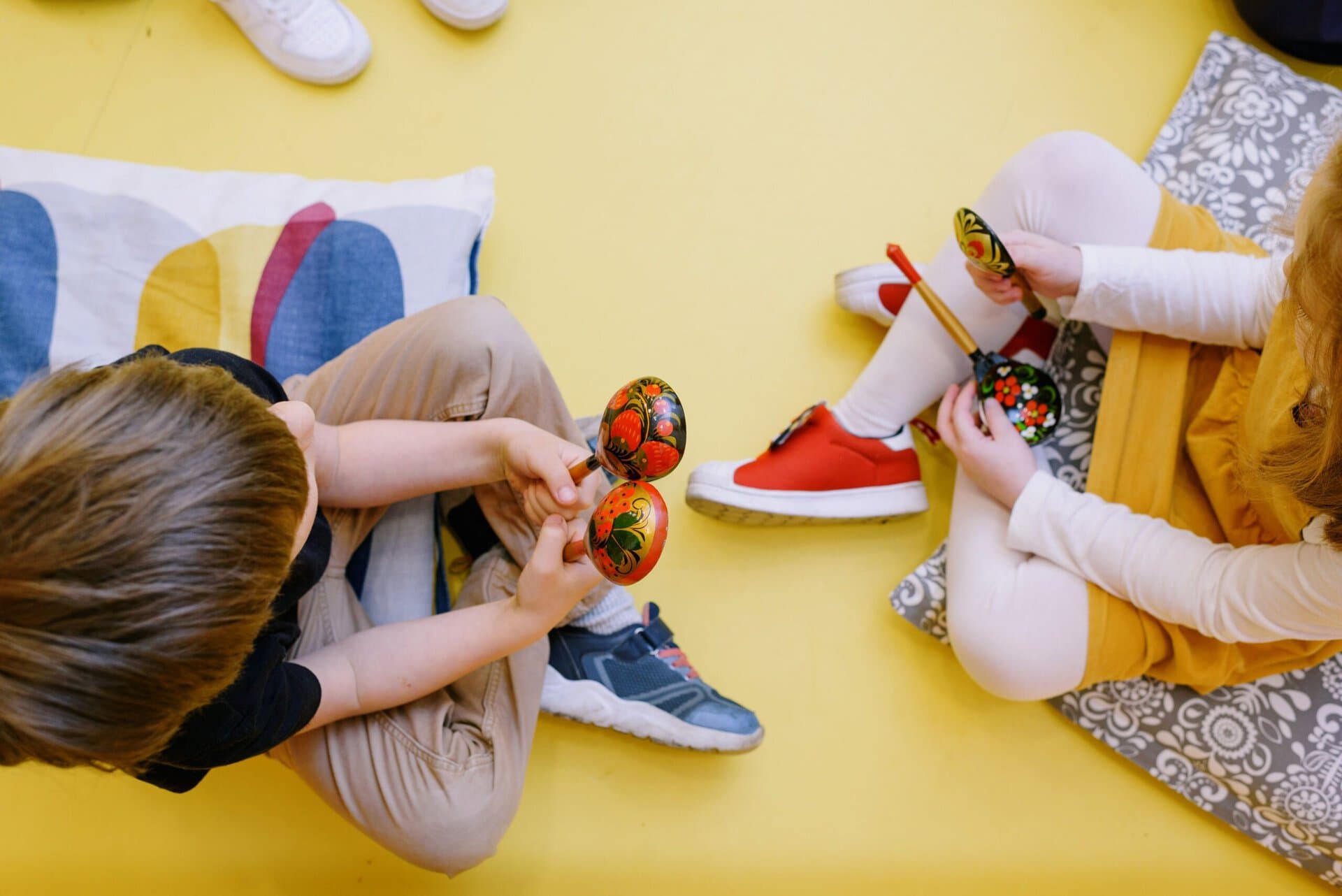 two children sitting on the floor playing with painted wooden spoons.