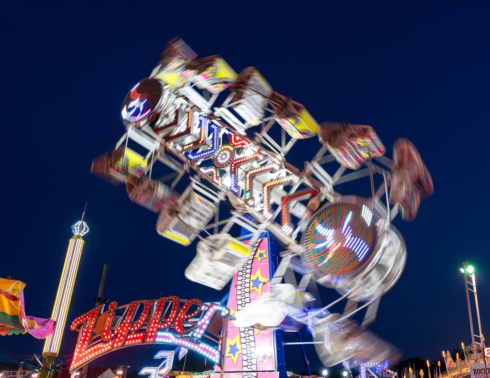 a brightly lit carnival ride spins rapidly at night, with colorful lights and motion blur, against a dark blue sky. a brightly lit carnival ride spins rapidly at night, with colorful lights and motion blur, against a dark blue sky.